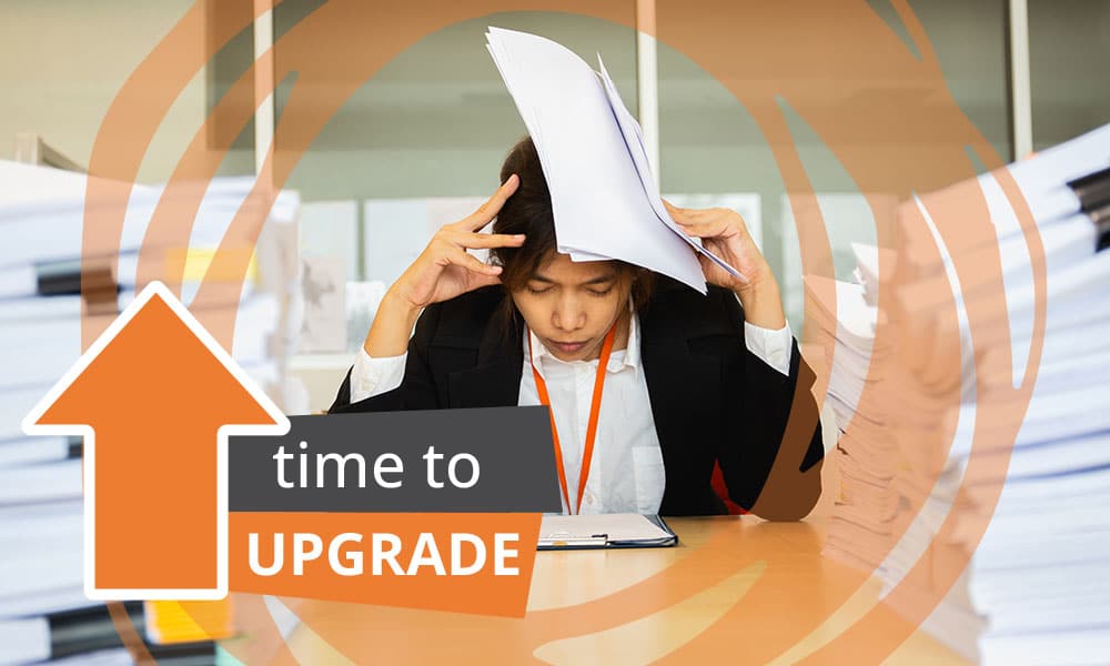 Image of office professional frustrated holding head, surrounded by piles of paper work. Image accompanying blog post about 11 Signs It's Time to Upgrade Your Grant Management Software in 2024